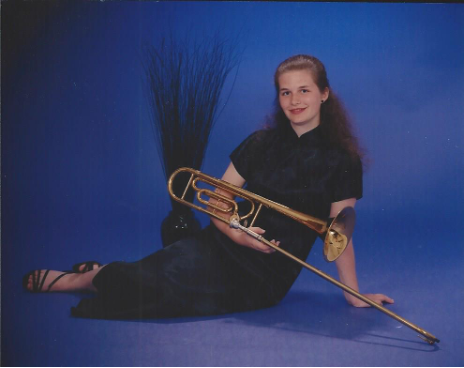 A picture of Katya wearing a qipao and posing with a trombone. 