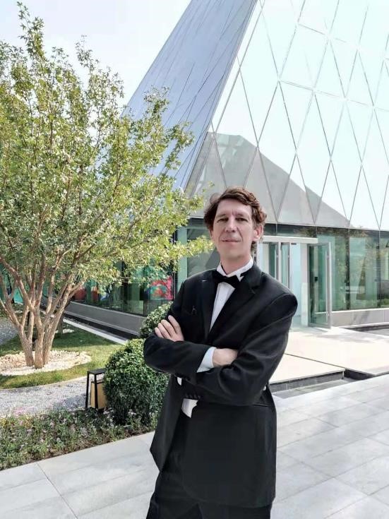 Bill wears a tuxedo and poses confidend in front of a modern theatre building.