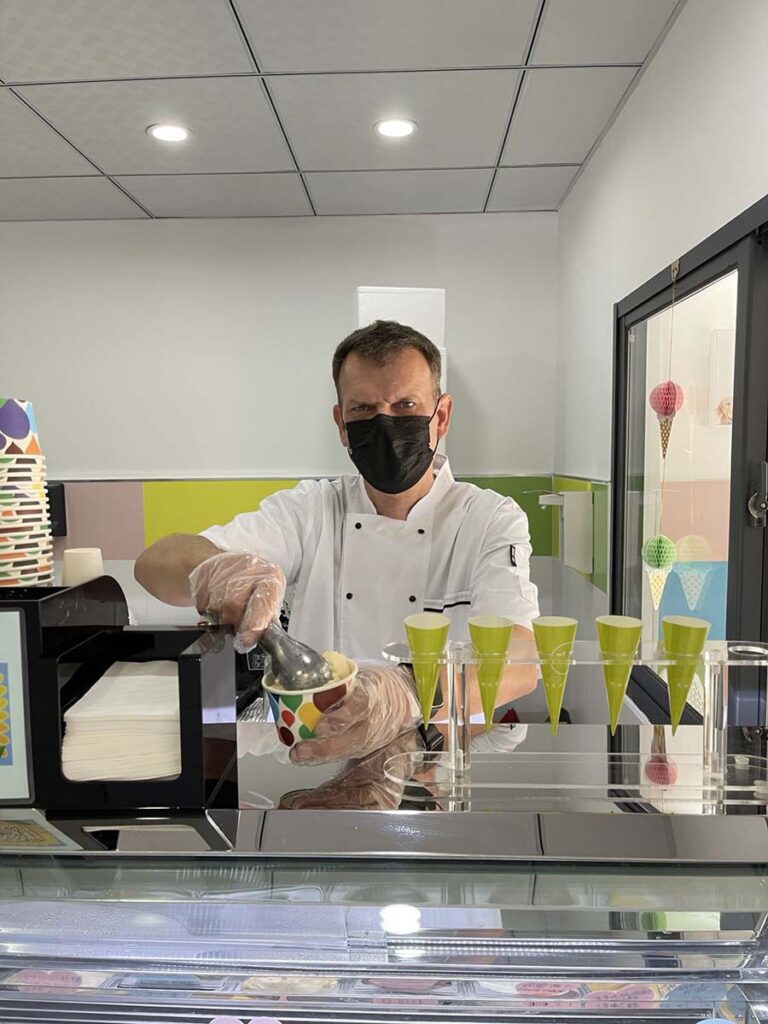 Andre wears a mask and protective gloves as he serves a scoop of delicious gelato in his store.